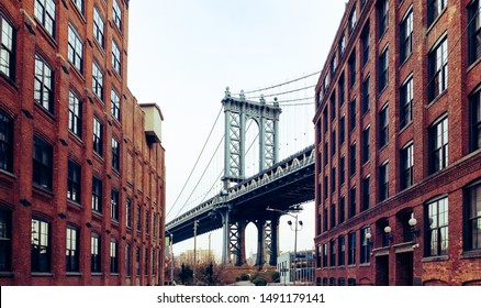 View of Manhattan Bridge viewed from Dumbo, Brooklyn, New York, USA. Landmark spot between two red brick buildings of iconic bridge of big apple city. Cloudy sky background of NY town.