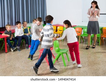 Happy kids and female teacher playing musical chairs together during break in classroom at elementary school