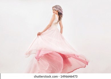 young girl with platinum long hair in a white pink dress is standing from the back like princess with skirt in flight and smiling cute on a white wall background. wedding queen concept, free space