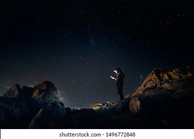 Der Mensch schaut mit seinem Scheinwerfer in der sternenklaren Nacht der Berge auf sein Telefon