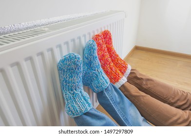 Familie in warme gebreide wollen sokken in de buurt van een huisverwarmer in koude wintertijd. Het symbolische beeld van het stookseizoen in huis. Een deel van het lichaam, selectieve aandacht.