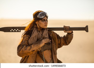Post-apocalyptic woman warrior with weapon outdoors. Attractive fichter girl in shabby clothes holding sword and binoculars standing in a confident pose looking away. People in nuclear post-apocalypse