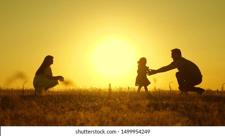 forældre leger med deres lille datter. mor og far leger med deres datter i solen. glad baby går fra far til mor. ung familie i marken med et barn 1 år. familie lykke koncept.