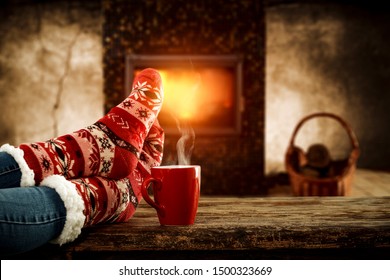 Woman legs with christmas socks and home interior with fireplace and dark wall background. Free space for your decoration. 