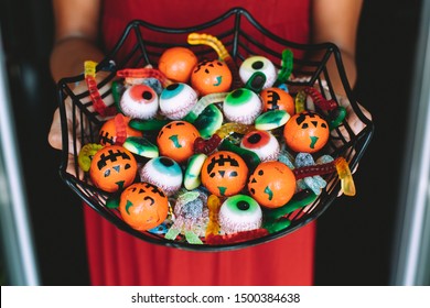 Woman at the front door offering funny Halloween candies on a spiderweb shaped bowl. Unrecognizable person