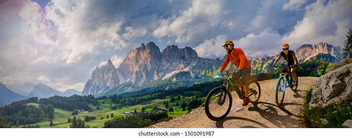 Parella amb bicicleta en bicicleta elèctrica, recorregut per sender de muntanya. Dona i home muntats en bicicleta al paisatge de les muntanyes de les Dolomites. Pista de ciclisme e-mtb enduro trail. Activitat esportiva a l’aire lliure.