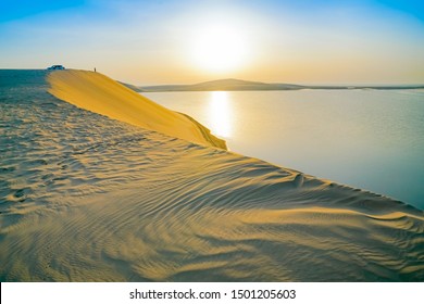 日の出の砂漠、カタールのドーハのすぐ外にあるシーライン砂漠の砂丘と内海の朝焼け。