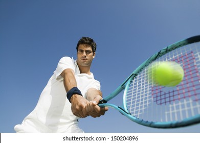 Lae hoekaansig van vasberade jong man wat tennis speel teen blou lug