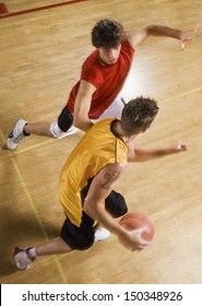 Pemandangan sudut tinggi dua pemuda bermain basket di lapangan dalam ruangan