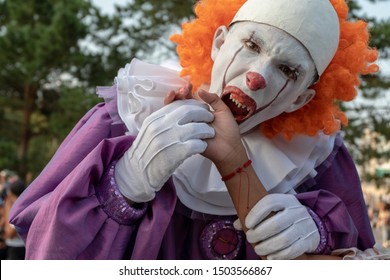 Cosplay de Halloween o festival de héroes de terror. Un adolescente con un disfraz de payaso malvado con dientes afilados finge morder la mano de alguien. Maquillaje de calle en un chico