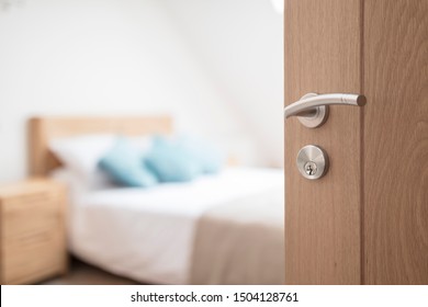 Drzwi do pokoju hotelowego lub apartamentu z kluczem i brelokiem w otwartych drzwiach oraz sypialnia w tle