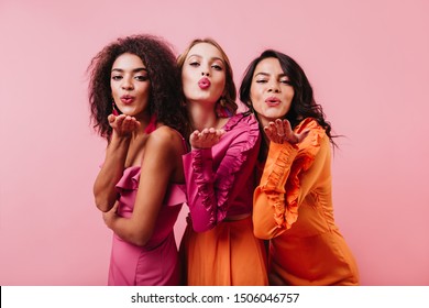 Grupo de mujeres enviando besos de aire sobre fondo rosa. Retrato de medio cuerpo de tres niñas de raza mixta.