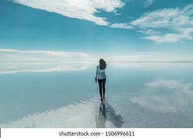Turis wanita & pantulan cermin yang indah di langit biru dan awan di Dataran Garam Bolivia. Ditembak di dataran garam Salar de Uyuni. Refleksi air dari awan dan ruang kosong. Liburan, adegan perjalanan liburan