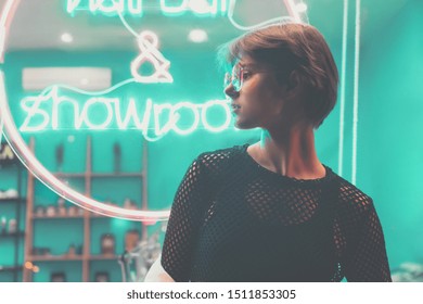 Hipster teen tomboy vajzë e bukur fytyrë të shkurtër me flokë të shkurtër veshin syze me stil në sfond shenjë neoni, blu rozë rrugë dritë rruge modës modës adoleshente modës shikimin e profilit të gruas së re në stilin e ndritshëm të qytetit