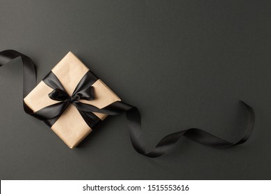 Caja de regalo artesanal sobre un fondo oscuro, decorada con un lazo texturizado y plumas, creando un ambiente romántico de lujo. Para cumpleaños, regalos de aniversario, postales de regalo.