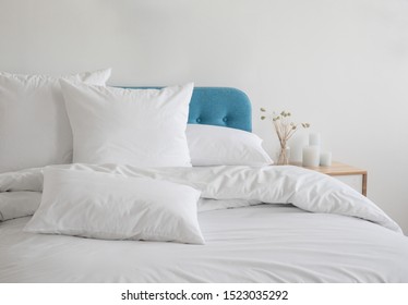White pillows, duvet and duvet case on a blue bed. White bed linen on a blue sofa. Bedroom with bed and bedding. Messy bed. Front view.