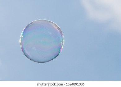 Burbuja iridiscente flotando en el aire en un día soleado cielo azul claro con una nube blanca. Diseño con espacio en el lado derecho para escribir mensajes de texto o citas célebres. La imagen sigue la regla de los tercios