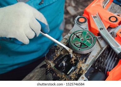 A man in blue clothes and work gloves is using a screwdriver to clean the chainsaw motor