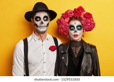 La aterradora pareja de muertos vivientes celebra la festividad mexicana para recordar a los parientes muertos, vestidos con disfraces de carnaval, usa maquillaje de calavera, flores rojas como símbolo de este evento. Los zombis se paran en el interior sobre la pared amarilla