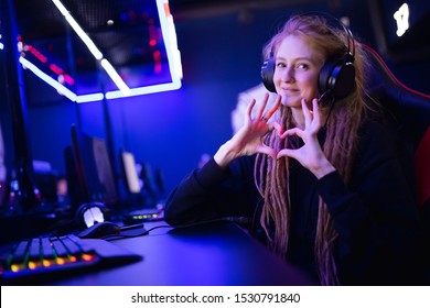 Streamer beautiful girl shows heart sign with hands professional gamer playing online games computer, neon color.