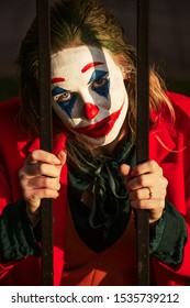 young woman with evil clown makeup and costume looking at camera through bars