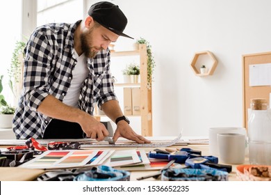 Un giovane creativo in abiti casual si china sul posto di lavoro mentre prepara i pezzi per collari decorativi per animali domestici in studio
