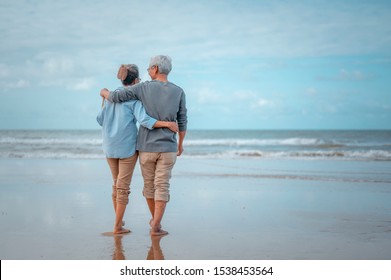 Las parejas mayores caminando por la playa en un día soleado, planean un seguro de vida con el concepto de jubilación feliz.