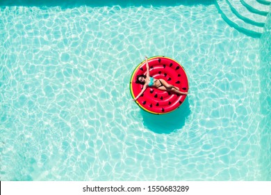 Aerial top of woman wearing a hat sitting in inflatable watermelon in deep cyan calm waters like a pool