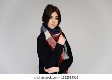 Close-up Portrait einer jungen hübschen Studentin mit langen schwarzen Haaren mit einem Schal und in einem Pullover, auf weißem Hintergrund. In verschiedenen Posen mit Emotionen direkt vor der Kamera stehen.