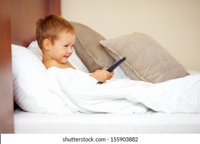 happy kid watching tv cartoons in bed