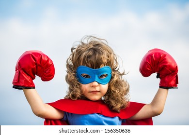 Superheldenkind, das Boxhandschuhe gegen Hintergrund des blauen Himmels trägt. Frauenpower und Feminismus Konzept