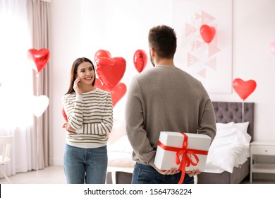 Jonge man presenteert cadeau aan zijn vriendin in slaapkamer versierd met hartvormige ballonnen. Valentijnsdag feest