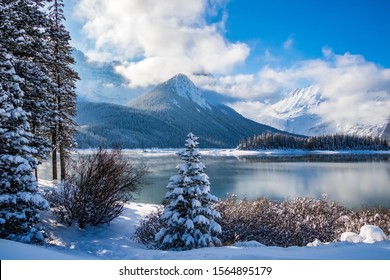 Landscaper view of a snowy shoreline against an unfrozen cold steamy lake with mountains in the background on a sunny day.