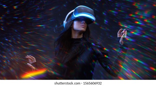 Grua e re e bukur duke përdorur përkrenare VR ndërsa prek ajrin në dritat shumëngjyrëshe neoni ylber. Vajza me gota realiteti virtual me dritë të pasme blu me flokë të rrjedhur mbi sfondin e errët të universit magjik.