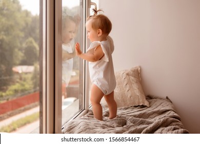 babymeisje 11 maanden staat op de vensterbank en kijkt uit het raam. warmte en comfort in huis. geluidsisolatie en kunststof ramen in huis