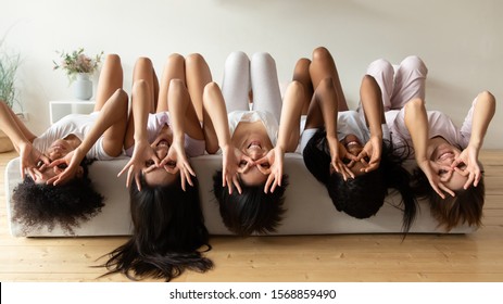 Cinco chicas divertidas y diversas usan pijamas acostadas en la cama boca abajo haciendo muecas mirando a la cámara, felices jóvenes mujeres multiétnicas divirtiéndose en el dormitorio disfrutando juntas de una fiesta de pijamas