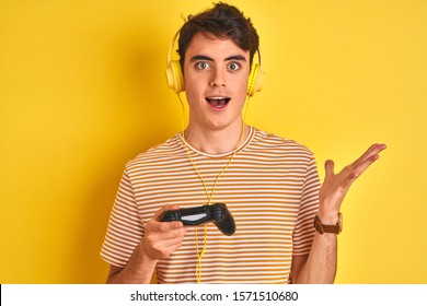 Teenager boy playing video games using gamepad over isolated yellow background very happy and excited, winner expression celebrating victory screaming with big smile and raised hands