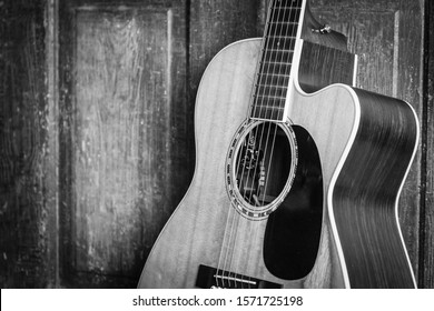 アコースティック ギターの美しいグレースケール ショットは、木製の表面に木製のドアにもたれかかっていた