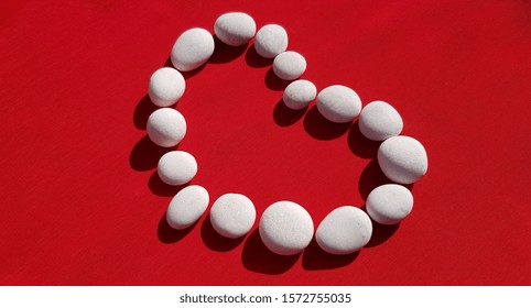 Silhouet van een hart van witte ronde stenen op rood (hoek, abstractie)