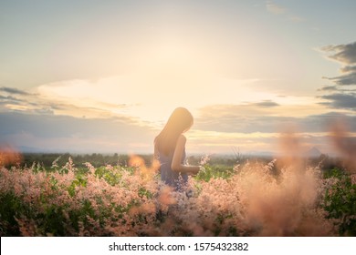 Trendiges Mädchen im stylischen Sommerkleid, das sich auf dem Feld mit Blumen im Sonnenschein frei fühlt.