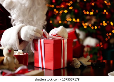 Papá Noel envolviendo el regalo de Navidad contra luces festivas borrosas, primer plano