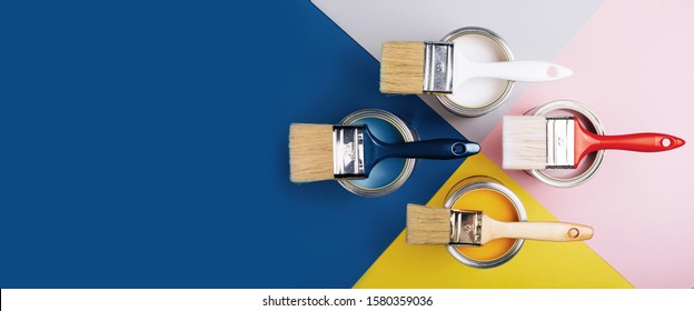 Banner con cuatro latas abiertas de pintura con pinceles sobre un fondo de simetría brillante. Colores de pintura amarillos, blancos, rosas y azules. Vista superior.