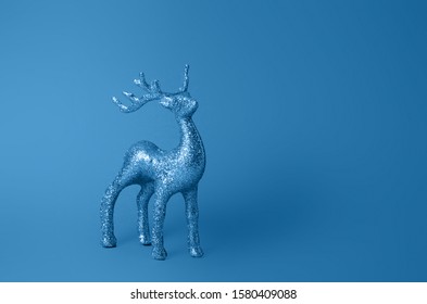 Sparkling deer decoration for Christmas. Deer figurine isolated on blue background. Christmas symbol. Decorations deer. Silver glitter stag decoration. Color of the year 2020 classic blue.