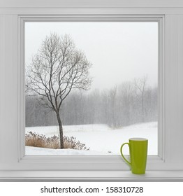 Groen theekopje op een vensterbank, met winterlandschap gezien door het raam.