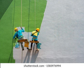 Dua orang pelukis sedang mengecat bagian luar gedung pada perancah yang tampak berbahaya yang tergantung di gedung tinggi dengan ruang fotokopi.