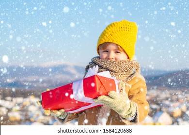 Semoga liburanmu menyenangkan. Anak musim dingin yang bahagia memegang hadiah latar belakang salju busur. Anak laki-laki lucu dengan topi pakaian musim dingin dan syal menutup. Selamat tahun baru dan selamat natal. Konsep liburan musim dingin.