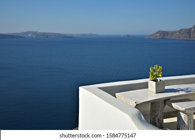 Porche tradicional de la casa con una mesa de patio de yeso de marfil hecha a mano y taburetes y un naranjo en miniatura con vistas a la caldera en la isla de Oia Santorini, Cícladas, Grecia.