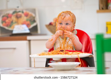 Unordentlicher kleiner Junge sitzt im Hochstuhl, bedeckt mit Spaghetti und Soße
