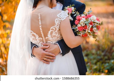 Petite bride in buttons back and butterfly back, pink powder color wedding dress is holding wedding bouquet with pink roses, the groom's arm around her waist, back view