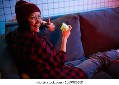 Teenager girl holding a smartphone while playing online shooting gaming. Thumbs up gesture.